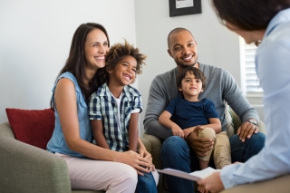 young multi-ethnic family mom and dad with children on laps, talking with realtor or lender at home